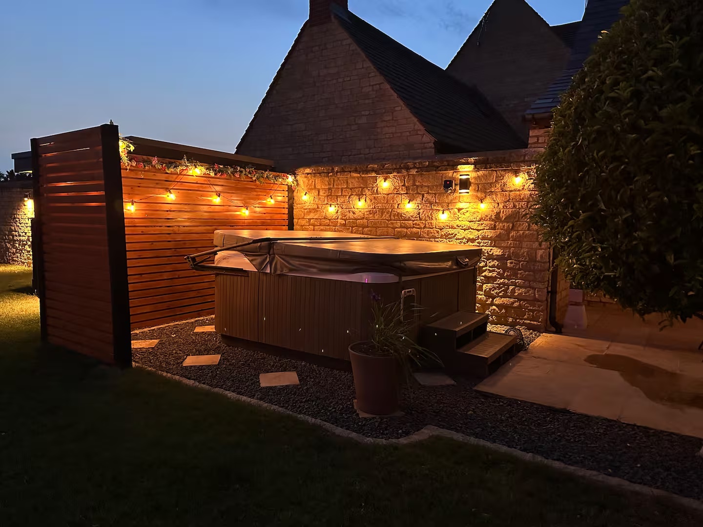 Hot tub beside the warmly lit stone wall at dusk