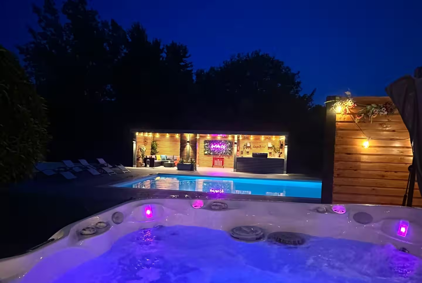 Private hot tub overlooking the illuminated pool and garden bar at night
