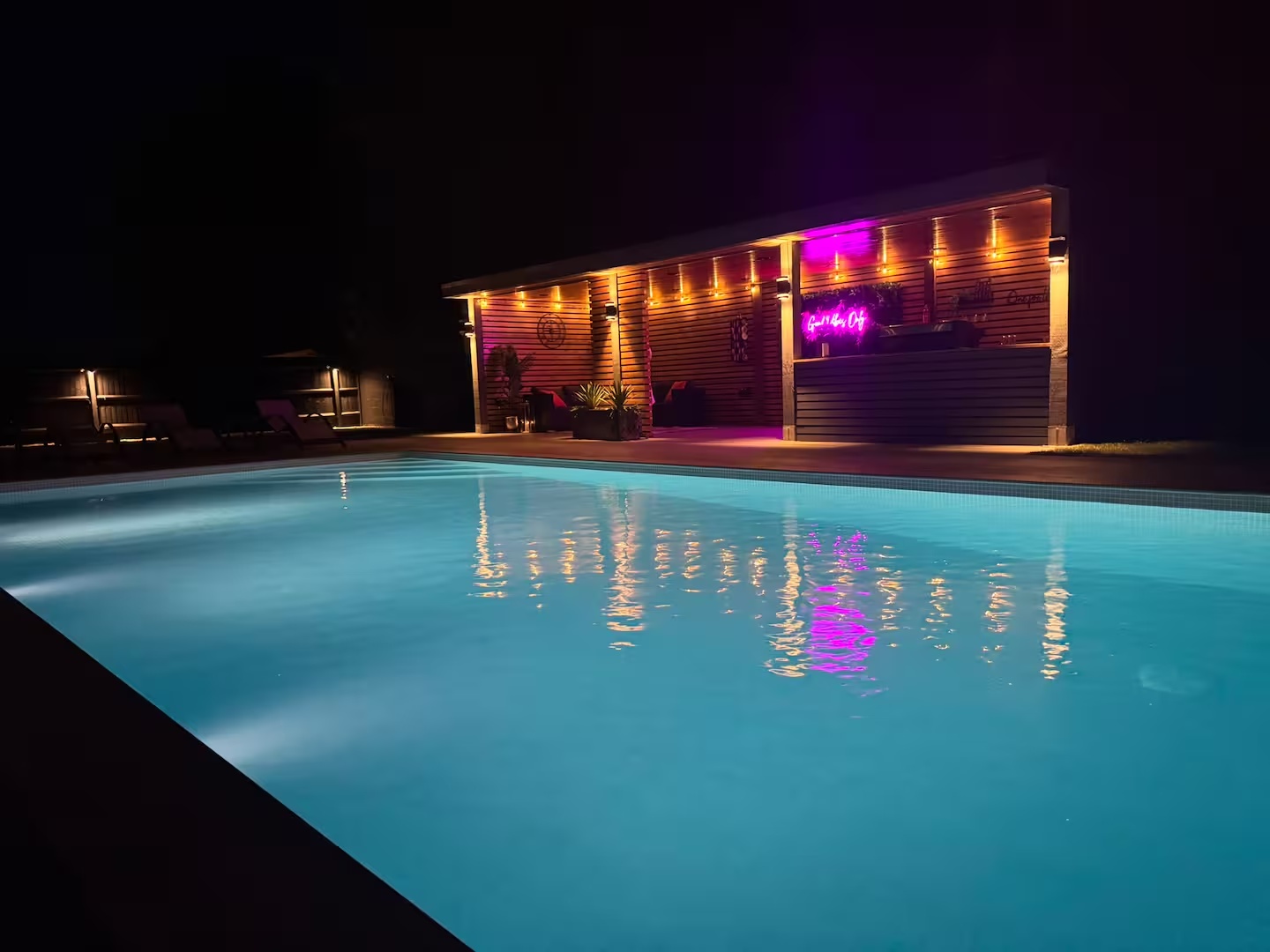Illuminated private pool reflecting the garden bar lights at night